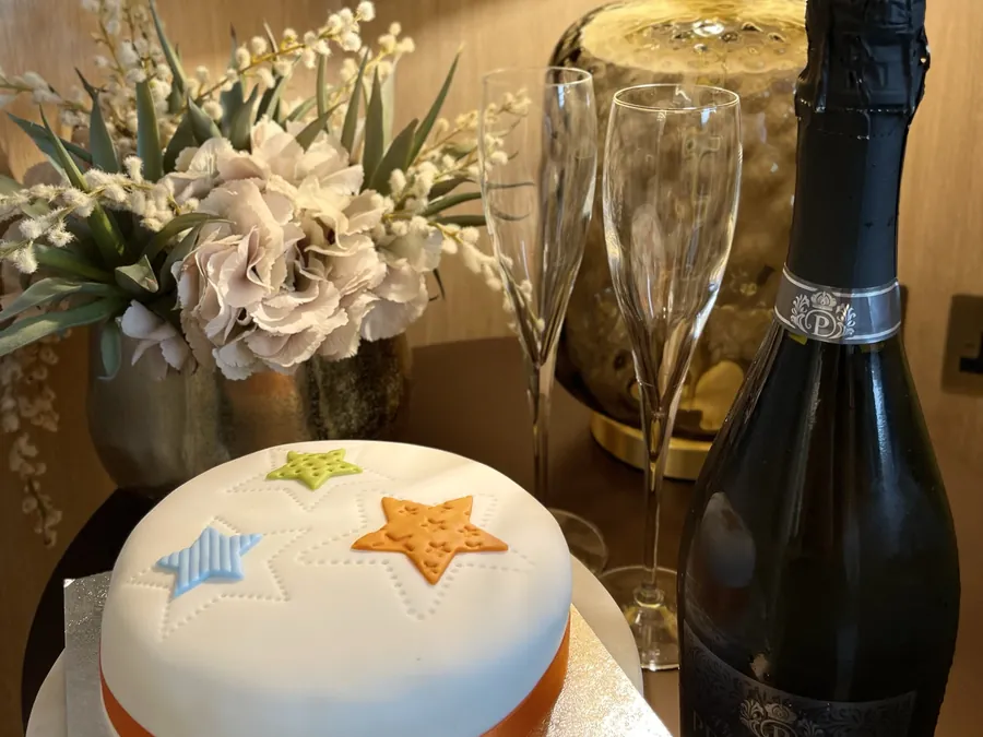 A celebration cake with a bottle of fizz and flowers