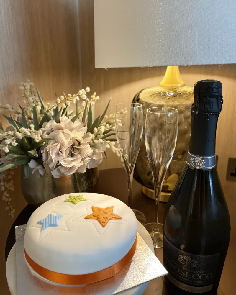 A celebration cake beside a bottle of fizz and white flowers