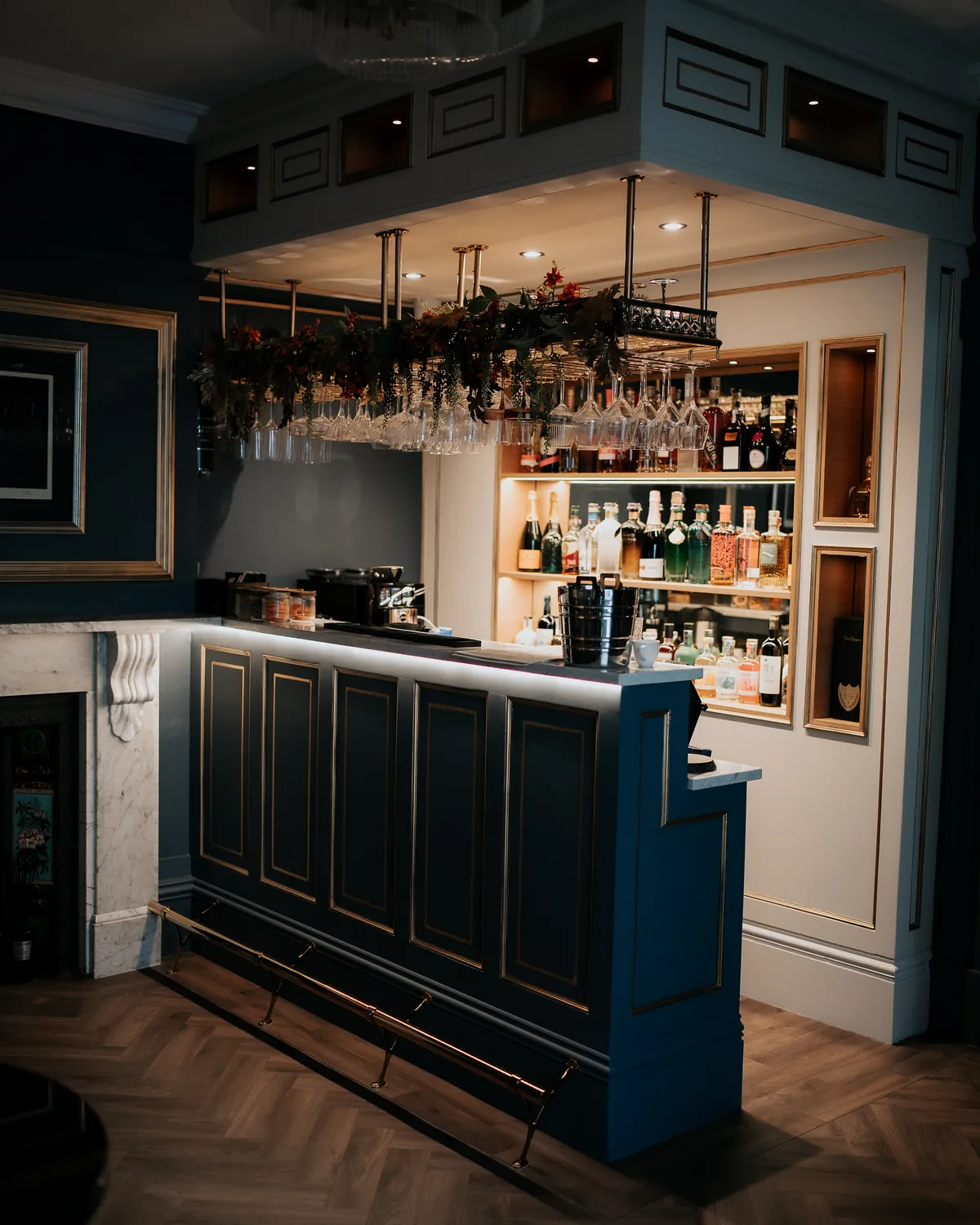 The bar in Nocturne: navy panelling with gold trim, glassware hanging above, bottles lit behind