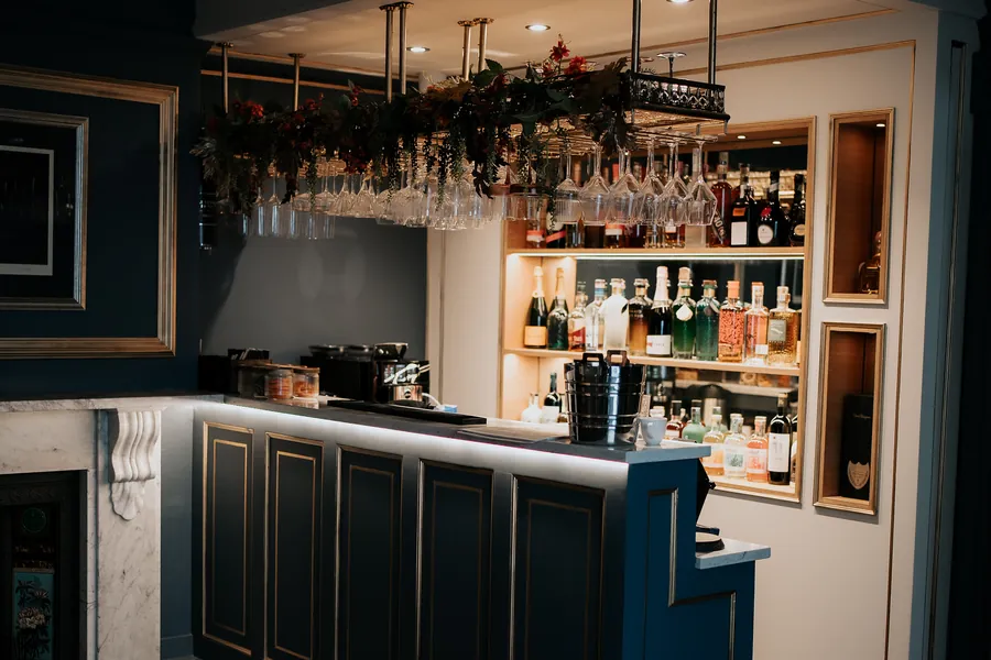 The bar in Nocturne with green panelling, hanging glassware and a wall of spirits