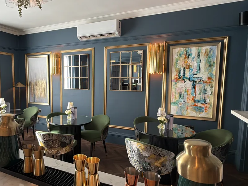 The lounge in Nocturne with deep blue walls, green velvet chairs and abstract art