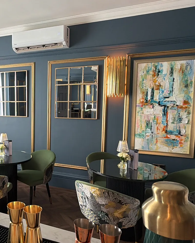 The lounge in Nocturne: deep blue walls, green velvet chairs and abstract art under low light