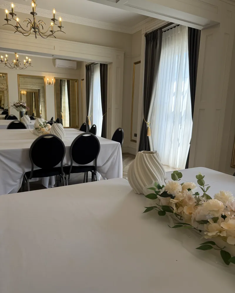 A white-clothed table in Orchidée with black chairs and white flowers, the chandelier above