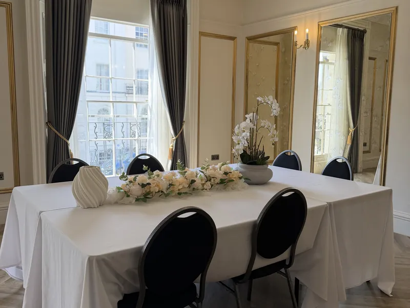 A long white table in Orchidée beneath the chandelier, with tall sash windows