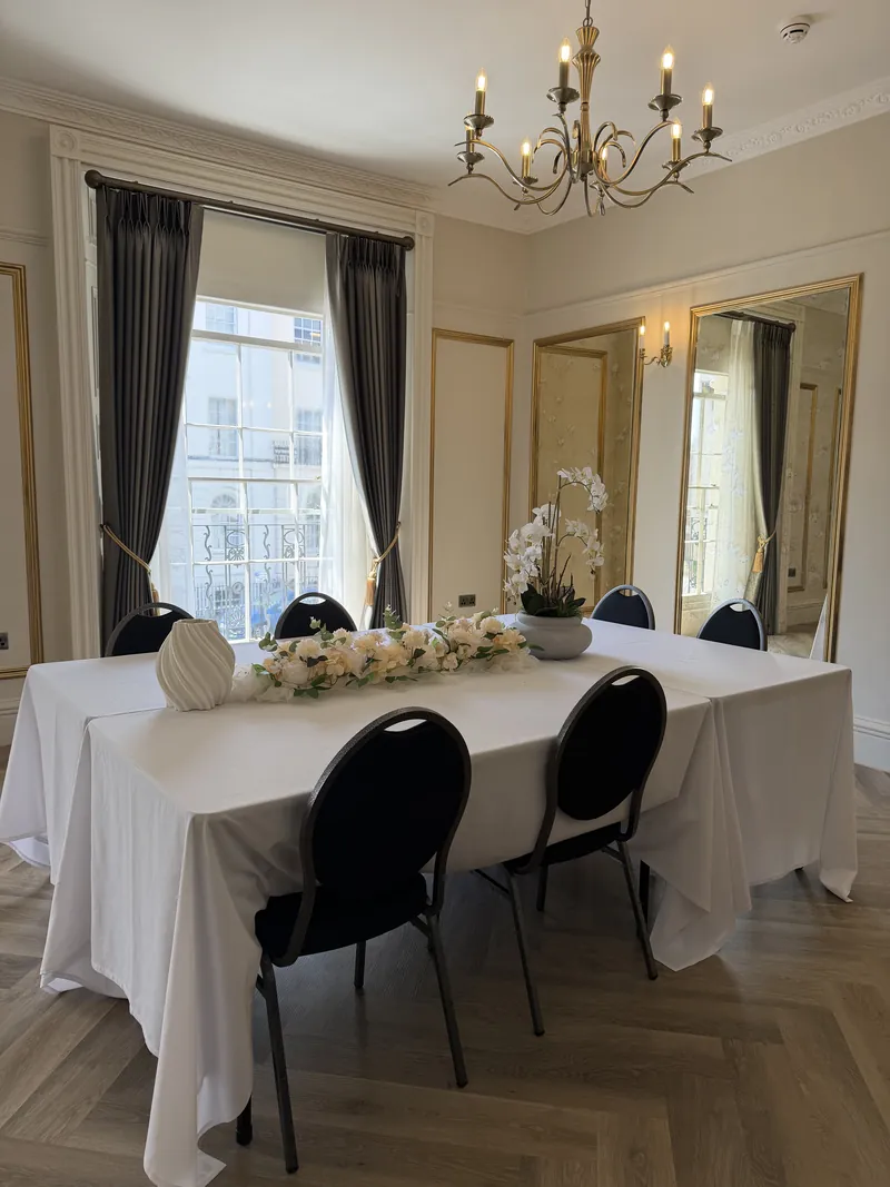 Orchidée: a long white table beneath the chandelier by tall sash windows