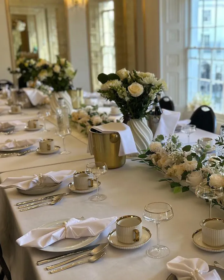 Gold cutlery, folded napkins and white flowers on a long table laid for dinner